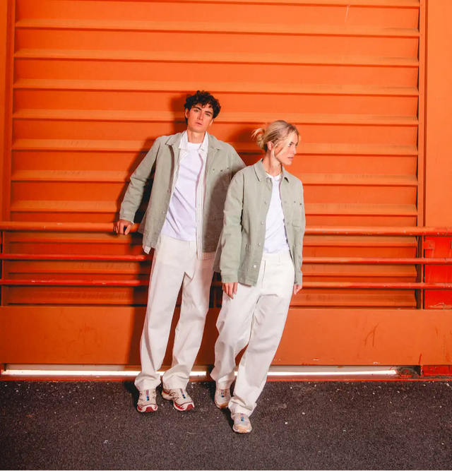 Deux jeunes adultes en tenues décontractées assorties composées de vestes vert clair, t-shirts blancs et pantalons écrus avec des chaussures de sport.