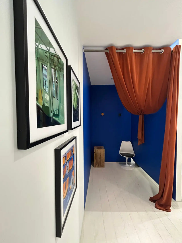 Un couloir bleu vif avec un rideau de couleur rouille menant à une chaise blanche.