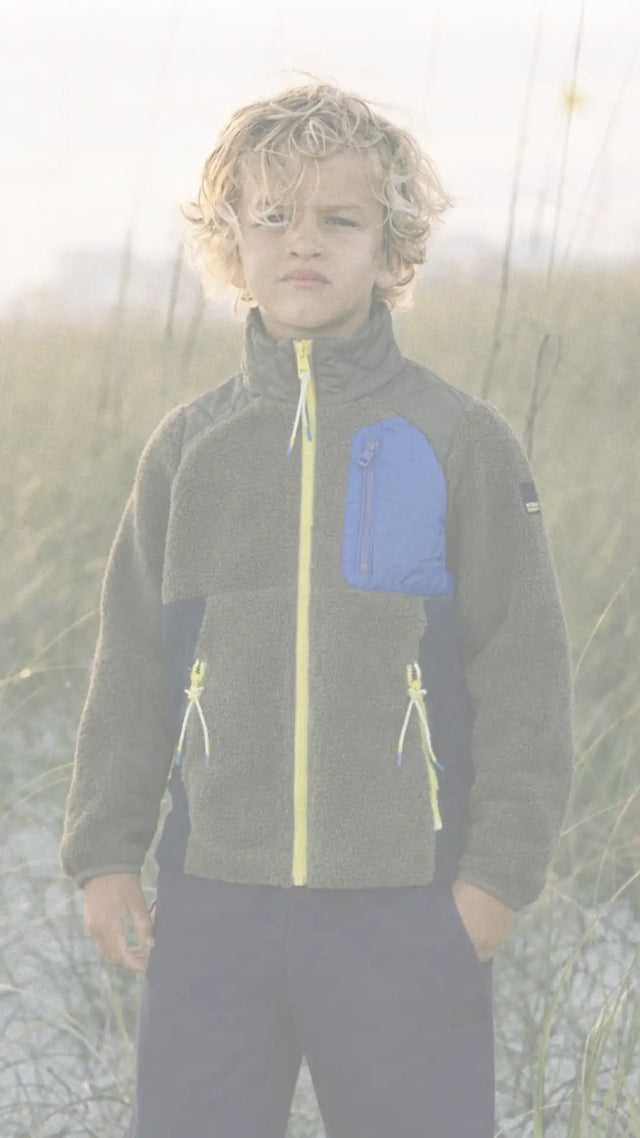 Un enfant portant une veste en polaire grise avec des accents bleu et jaune.