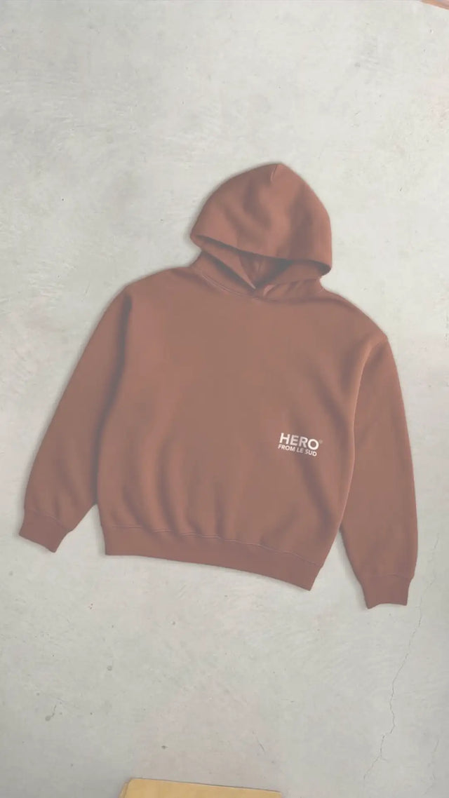 Sweat à capuche marron avec le texte « hero » sur la poitrine, probablement fabriqué en coton ou en mélange de polyester.